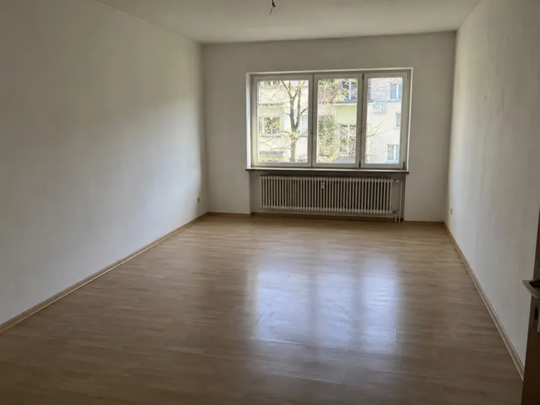Ein leerer Wohnraum mit Laminatboden, Fensterfront und Heizkörper.