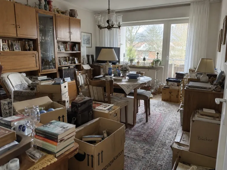 Esstisch, Schrankwand, Umzugskartons und persönliche Gegenstände in einer Wohnung.